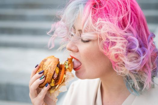 Caucasian woman with curly colored hair eating burger. Bad eating habits and love of fast food.