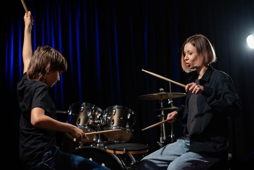 Young caucasian woman teaches a boy to play the drums in the studio on a black background. Music school student.