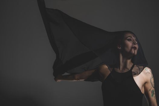 Redhead woman with a black veil on her head in a dark studio. A girl with an earring in her nose smiles slyly. Witch Makeup. Halloween costume