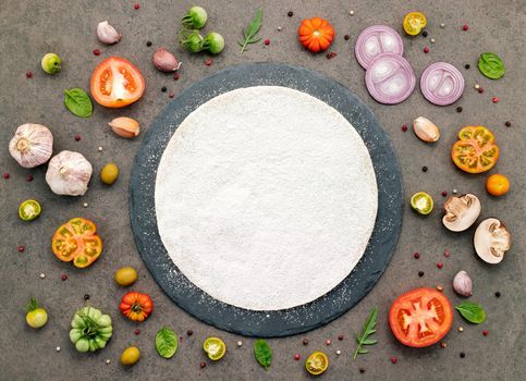 The ingredients for homemade pizza set up on dark stone background.