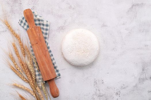 Wheat ears and wheat grains setup with rolling pin on white concrete background.