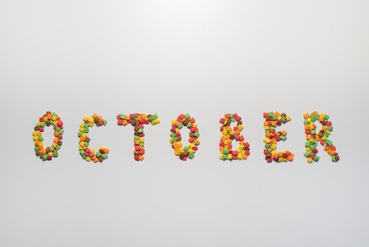 October inscription on a white background. Confectionery sprinkles in the form of multi-colored maple leaves.