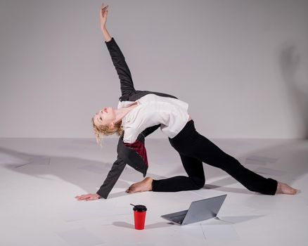 Barefoot ballerina dressed in a business suit poses for a laptop and drinks coffee. Flexible woman works at the computer.