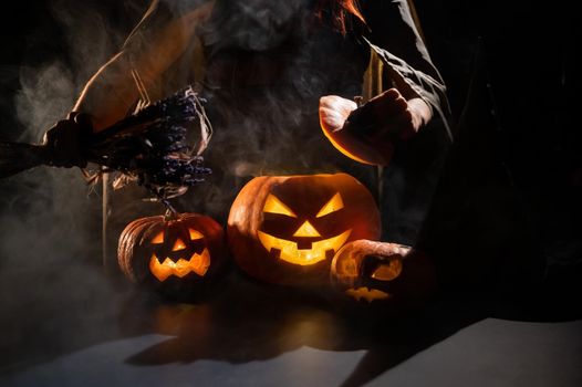 Witch casts a spell on a steaming pumpkin in the dark on Halloween.
