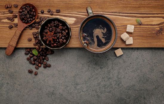 Roasted coffee beans with coffee cup setup on dark stone background.