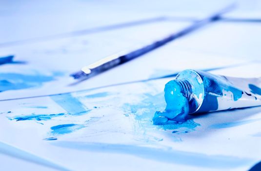 Opend blue watercolor tube  with paint brush white  background with spots of color