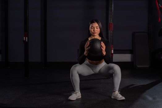 Asian woman squatting with a medicine ball in the gym