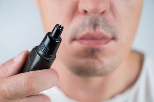 A man cuts his nose hair with a pocket trimmer.