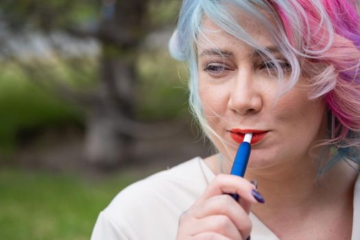 Caucasian woman with colored hair smokes an electronic cigarette