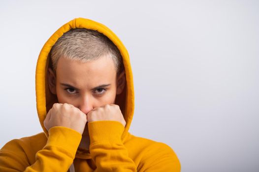 Young woman in ocher hood holding fists near face on white background