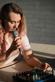 A woman sings into a microphone and plays online. A female blogger is recording a song using a synthesizer with a laptop