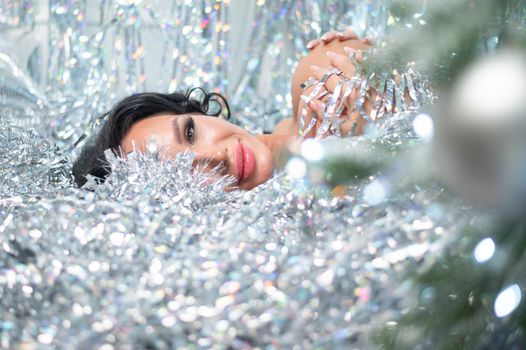 Caucasian nude woman lies in Christmas tinsel rain.