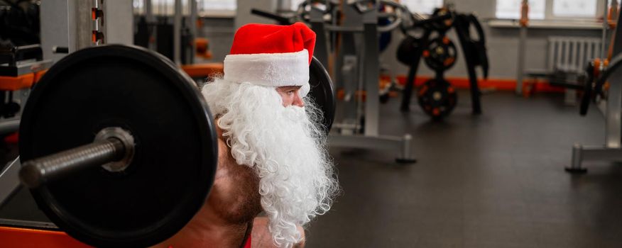 Santa claus in the gym. Muscular man with a naked torso doing exercises with dumbbells
