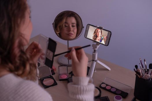 Caucasian woman leads an online make-up lesson for herself on her mobile phone.