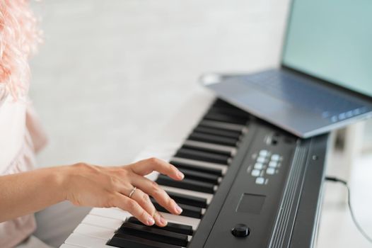 The woman plays the synthesizer and looks at the laptop screen. Close-up of female hands on the electric piano