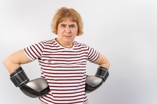 Elderly woman in fighting gloves in a defensive pose on a white background