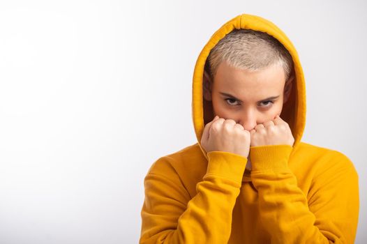 Young woman in ocher hood holding fists near face on white background