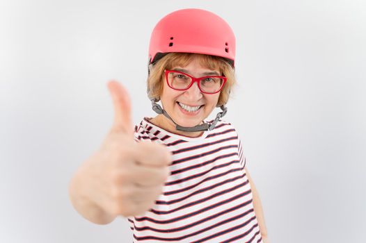 Elderly woman in ski helmet showing thumb up on white background