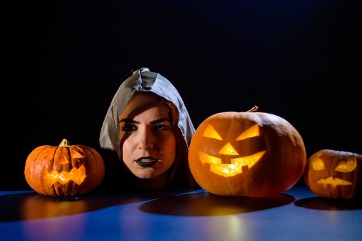 The evil witch casts a spell on pumpkins. Portrait of a woman in a carnival halloween costume in the dark.