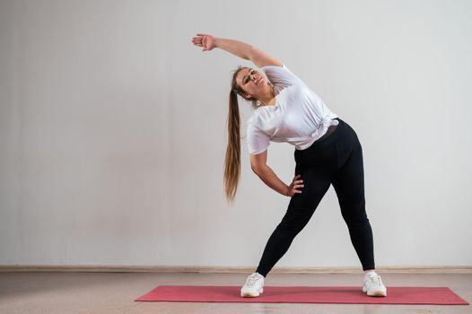 Young fat woman doing flexibility exercises on a white background.