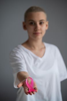 A faceless woman wearing a white t-shirt holds a pink ribbon as a symbol of breast cancer on a white background
