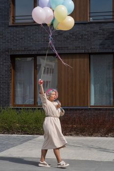 Woman in colored hair walks with an armful of balloons and drinks a refreshing beverage.