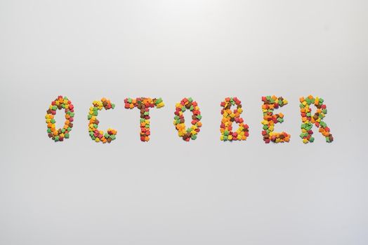 October inscription on a white background. Confectionery sprinkles in the form of multi-colored maple leaves.