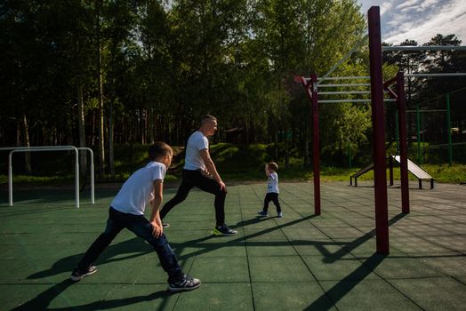 Caucasian man and two boys doing exercises outdoors. Father and sons train on the sports ground.