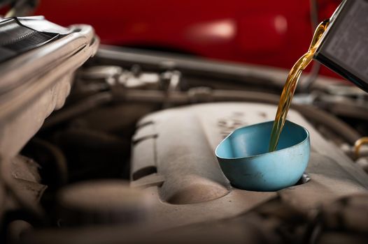 Auto mechanic pours oil into a car engine