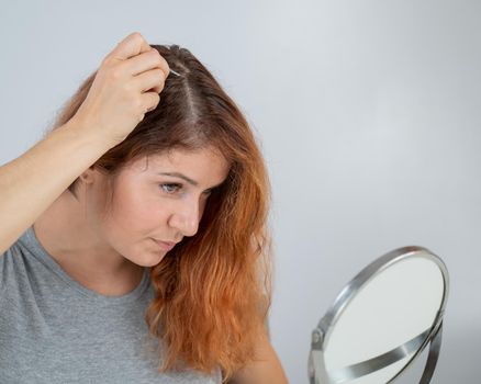 Caucasian woman finds gray hair and removes it with tweezers. Signs of aging