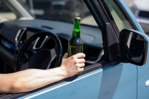 A faceless woman is drinking a bottle of beer while driving a car. Breaking the law and drinking alcohol while driving.