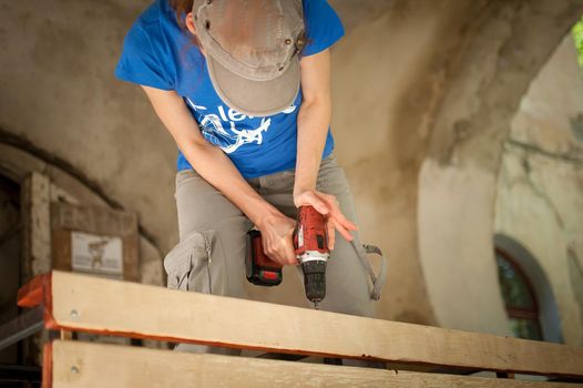 Skilled young female worker is using power screwdriver drilling during construction wooden bench gender equality, feminism, do it yourself concepts