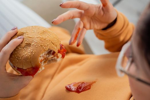 Caucasian young woman eating burger and getting dirty in ketchup. Sloppy girl.