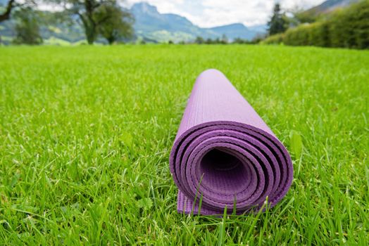 Rolled up fitness mat on the green grass background. Switzerland Alps. Outdoor training concept