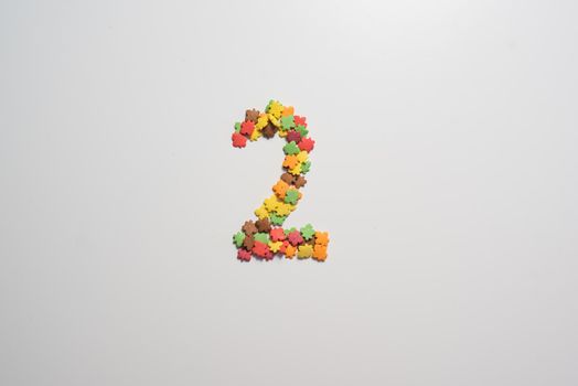 Numeral two from sweet pastry topping in the form of colorful foliage on a white background