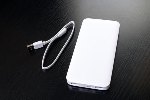 White power bank and cable on black wooden table