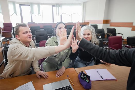 Students and lecturer give a high five in the university classroom