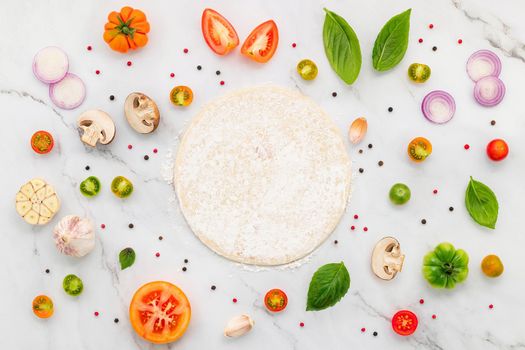 The ingredients for homemade pizza set up on white marble background.