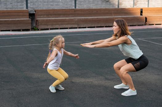 Mother and daughter go in for sports outdoors. Caucasian woman and little girl are engaged in fitness at the stadium