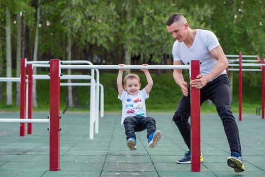 Caucasian man trains a boy on the uneven bars on the playground. Dad and son go in for outdoor sports