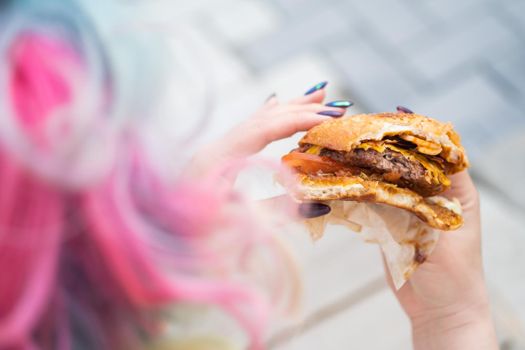 Caucasian woman with curly colored hair eating burger. Bad eating habits and love of fast food.