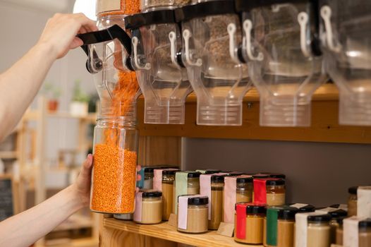 A man fills a jar with red lentils. Selling bulk goods by weight in an eco store. Trade concept without plastic packaging.