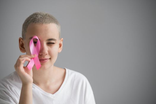 Young woman with short hair wearing a white t-shirt holding a pink ribbon as a symbol of breast cancer on a white background