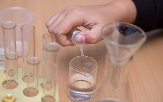 Close-up of a student's hand dripping a chemical solution into a glass. A schoolboy performs a task at the workplace. The concept of children's education, teaching knowledge, skills and abilities.