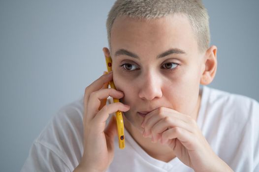 A pensive young woman with a short haircut talks thoughtfully on a mobile phone on a white background.