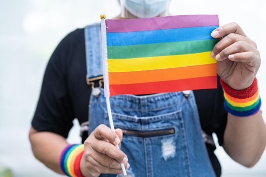 Asian lady wearing blue jean jacket or denim shirt and holding rainbow color flag, symbol of LGBT pride month celebrate annual in June social of gay, lesbian, bisexual, transgender, human rights.