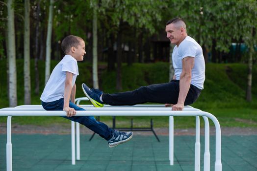 Caucasian man trains a boy on the uneven bars on the playground. Dad and son go in for outdoor sports