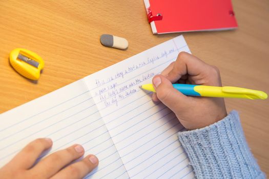 Close-up pupil's hands are writing in English in a notebook. A schoolboy performs a task at the workplace. The concept of children's education, teaching knowledge, skills and abilities.