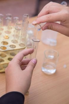 Close-up pupil's hands pouring liquid from a chemical test tube. A schoolboy performs a task at the workplace. The concept of children's education, teaching knowledge, skills and abilities.