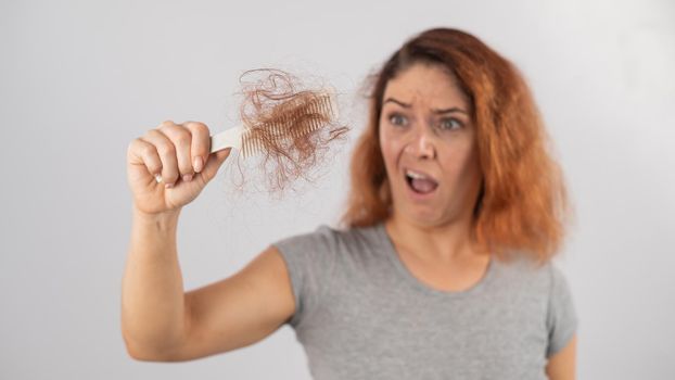 Caucasian woman with a grimace of horror holds a comb with a bun of hair. Hair loss and female alopecia